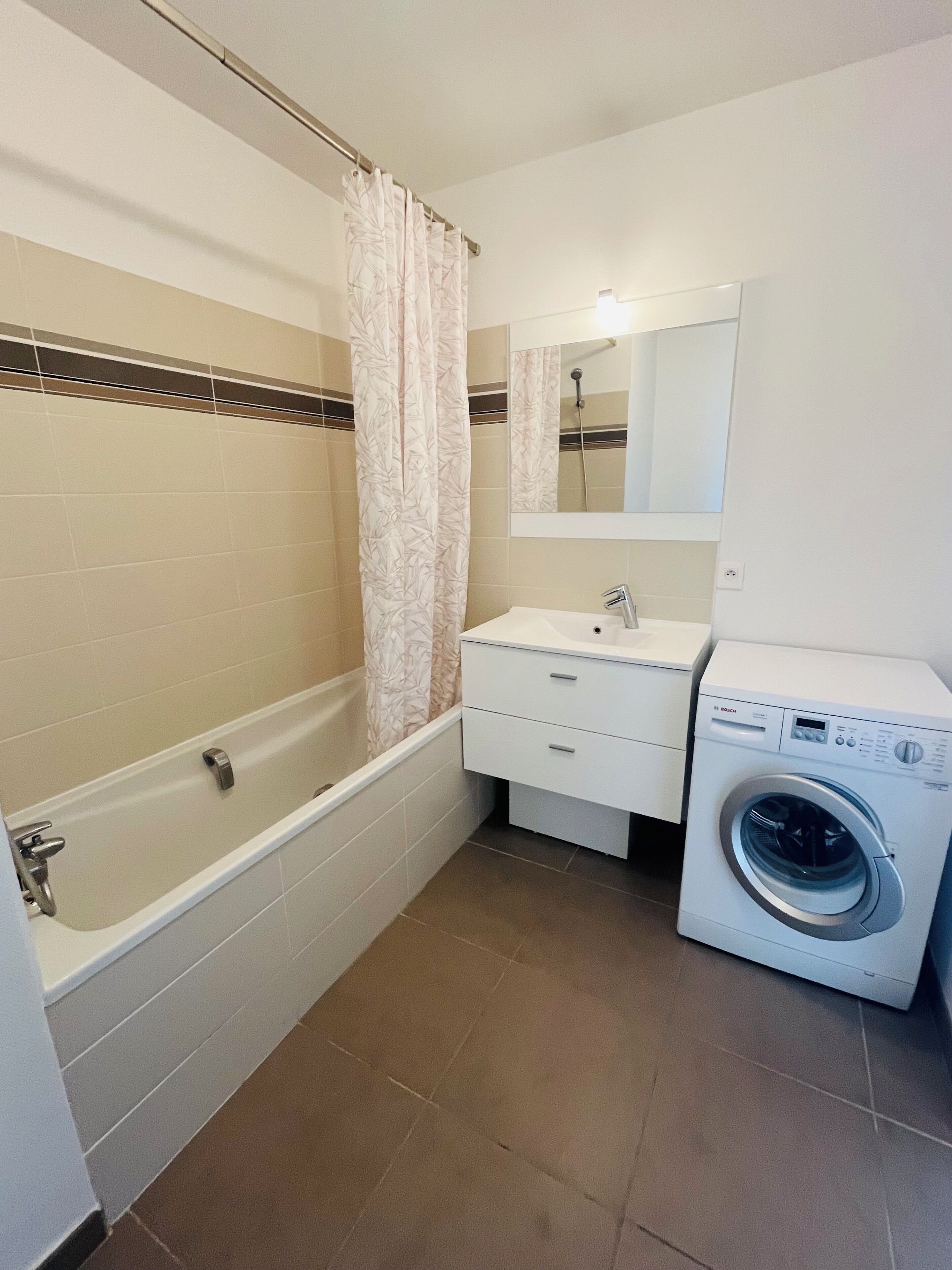 A bathroom with a bathtub, a shower, a sink, a mirror, and a washing machine.