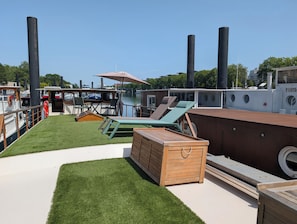 A boat deck with artificial grass, lounge chairs, a wooden bench, and a bar area.