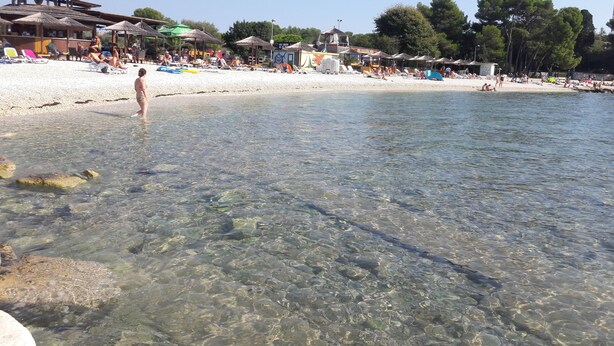 Ein Strand mit klarem, flachen Wasser, Sonnenschirmen und entspannten Menschen.
