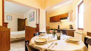 Ein Essbereich mit Tisch für zwei, eine Küche im Hintergrund und ein Bett im angrenzenden Zimmer.