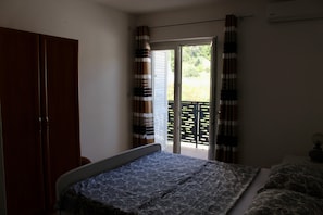 A bedroom with a bed, a wardrobe, and a balcony with curtains. - One Bedroom Apartment with Balcony and Mountain View (Baška Voda)