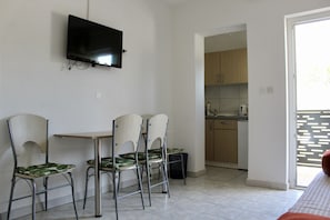 A dining area with a TV mounted on the wall, a small table, and three chairs with green leaf patterns. - One Bedroom Apartment with Balcony and Mountain View (Baška Voda)