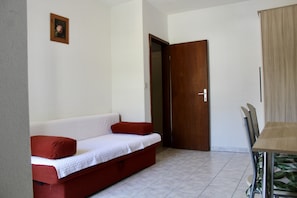 A room with a red sofa, a wooden door, and a dining table with chairs. - One Bedroom Apartment with Balcony and Mountain View (Baška Voda)