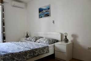 A bedroom with a bed, bedside tables, a wall-mounted air conditioner, a painting, and a power outlet. - One Bedroom Apartment with Balcony and Mountain View (Baška Voda)