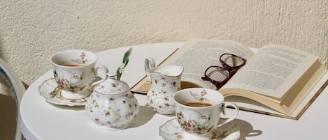 A round table with a white teapot, two cups, a pitcher, and a book with glasses on it.