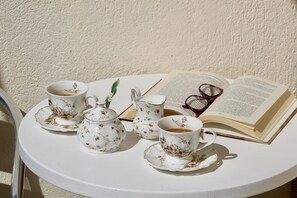 Ein runder Tisch mit einer weißen Teekanne, zwei Tassen, einer Kanne und einem Buch, auf dem Brillen liegen.