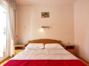 A bedroom with a bed, two bedside tables, a nightstand, a window with curtains, and a wall-mounted light fixture. - Family Apartments Stefani (Vodice)
