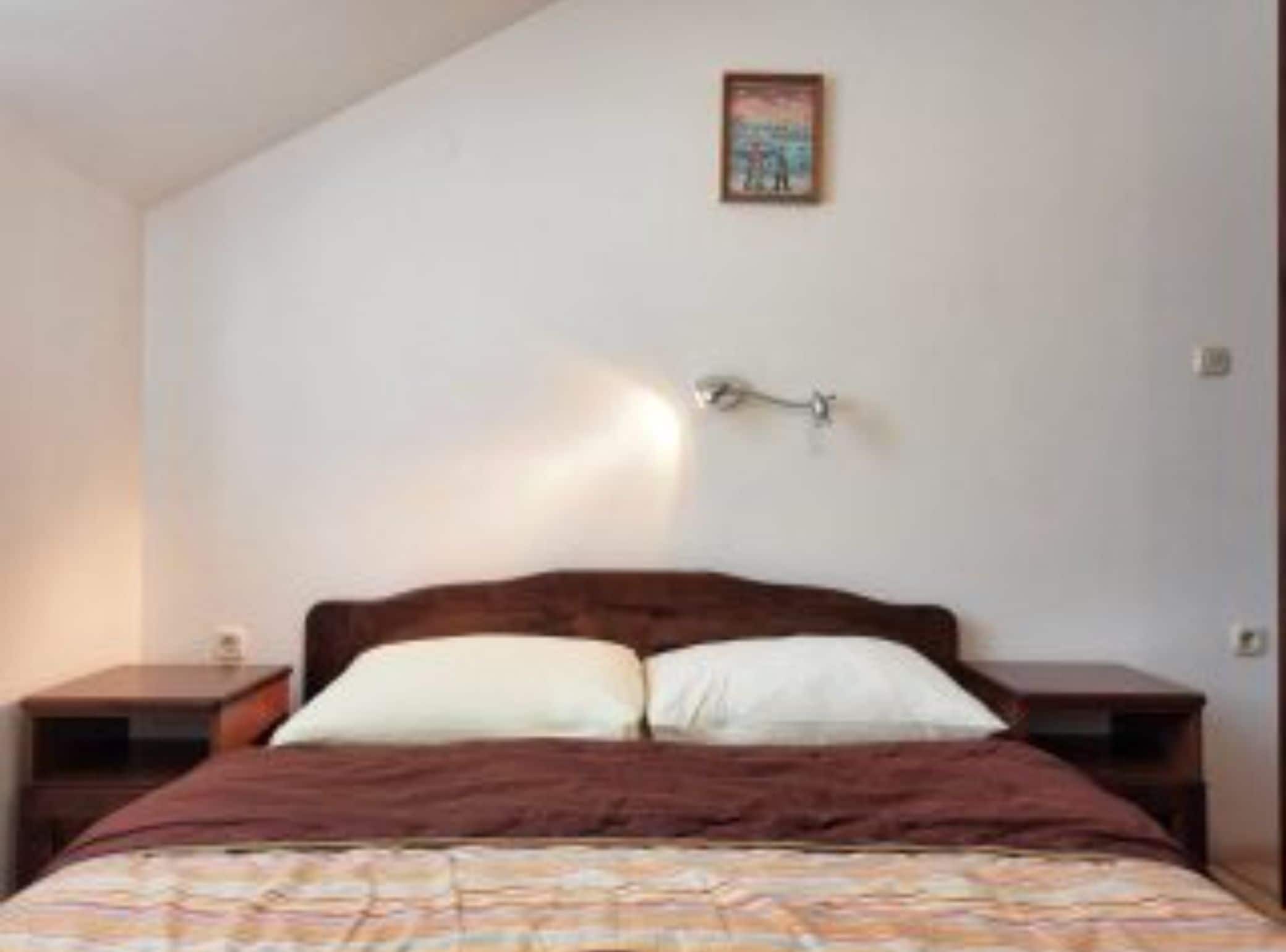 A bedroom with a bed, two bedside tables, a wall-mounted lamp, and a framed picture on the wall.