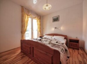 A bedroom with a wooden bed, a nightstand, a wall-mounted light, and a window with curtains. - Family Apartments Stefani (Vodice)