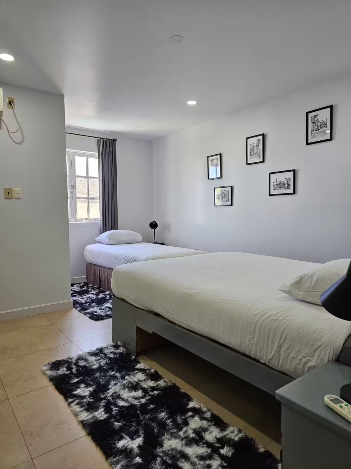 Ein Schlafzimmer mit einem Bett, einem Nachttisch, einer Lampe, einem Teppich und gerahmten Bildern an der Wand.
