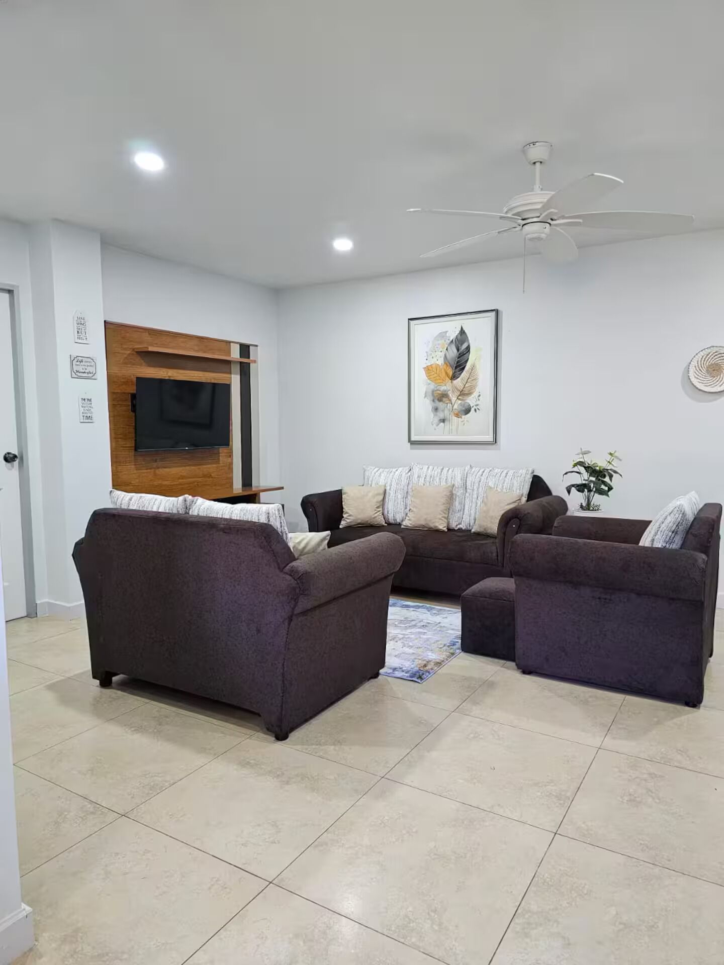 A living room with a sectional sofa, a flat-screen TV, a ceiling fan, and a framed artwork on the wall.