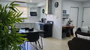 A modern kitchen with white cabinets, a dining area with a table and chairs, and a living room with a sofa.