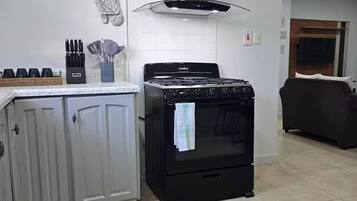 Una cucina con piano cottura, forno e zoccolo. Si vedono armadietti, una sveglia e un appendi-asciugamani a parete.