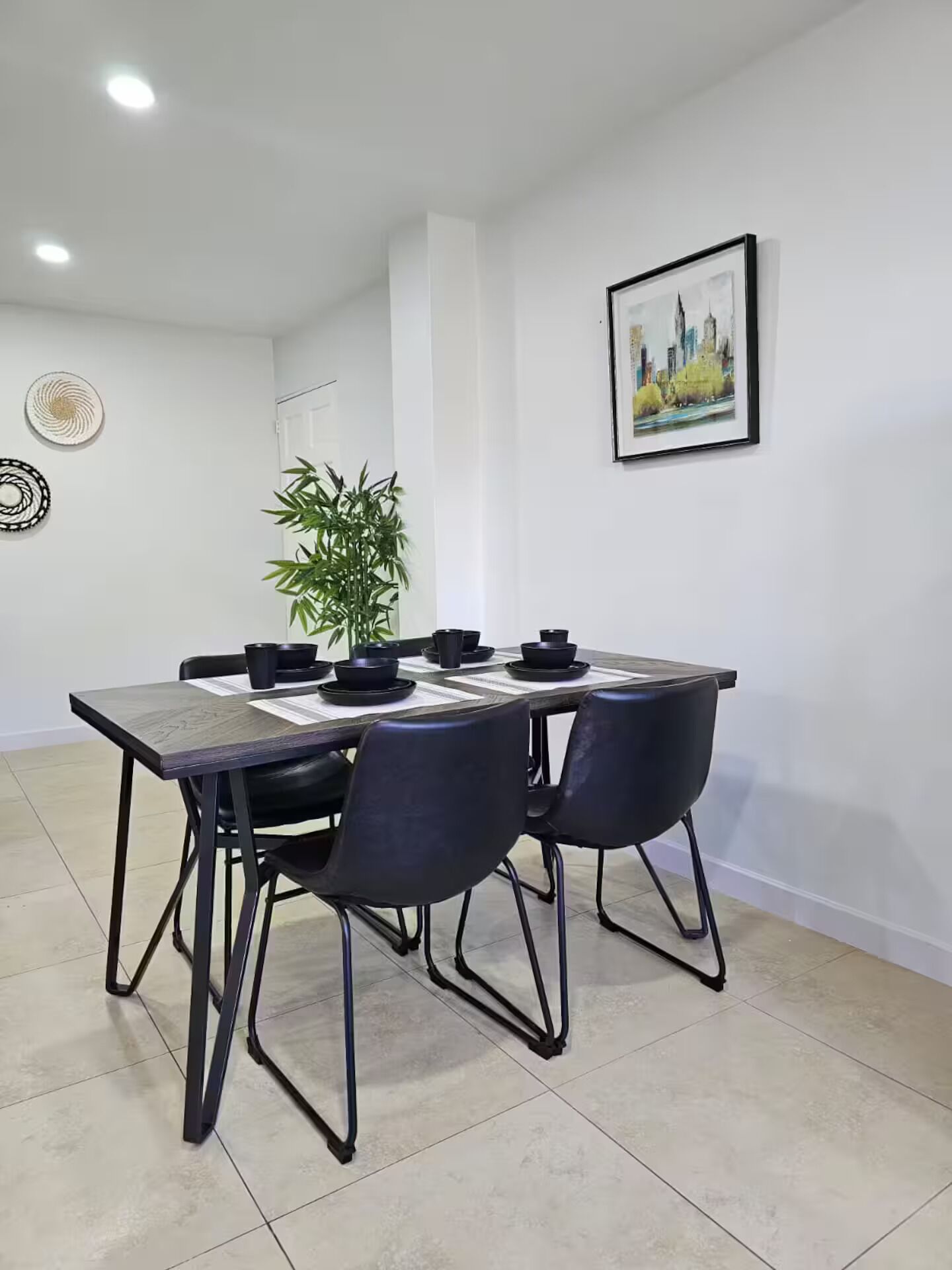 A dining area with a table, chairs, a plant, and a framed picture on the wall.
