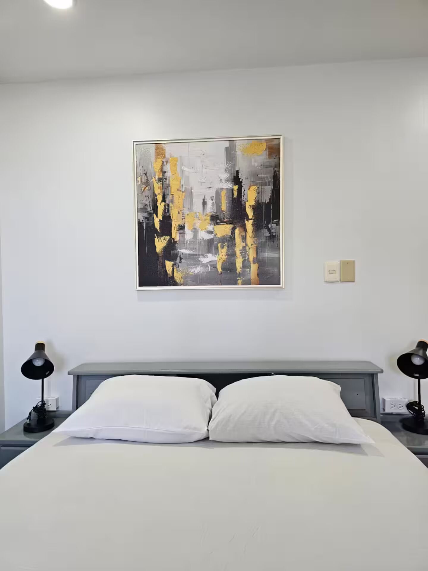 Una habitación de hotel moderna con un cuadro abstracto grande, una cama bien hecha y dos lámparas de noche.