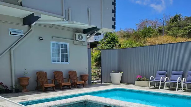 A swimming pool with a stone border, outdoor chairs, and a building with air conditioning units.