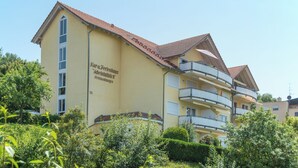 Um hotel de vários andares com varandas, telhado em telhas e uma placa indicando que é uma propriedade para aluguel.