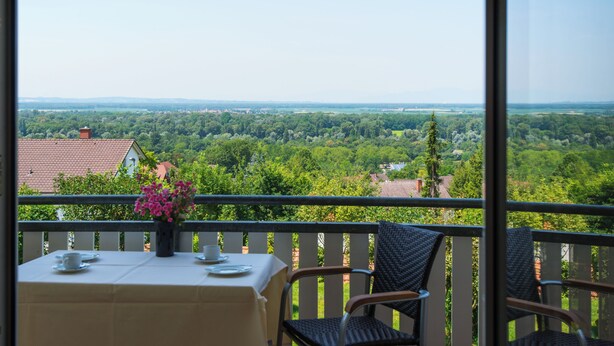 Varanda com mesa posta para dois, com vista para uma paisagem verde exuberante.