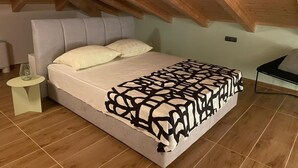 A bedroom with a sloped ceiling, a bed with a patterned bedspread, a bedside table, and a chair. - Apartment Niccolo - Duplex Apartment with Sea View (Fazana)