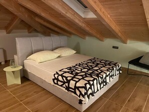 A bedroom with a sloped ceiling, a bed with a patterned bedspread, a bedside table, and a chair. - Apartment Niccolo - Duplex Apartment with Sea View (Fazana)