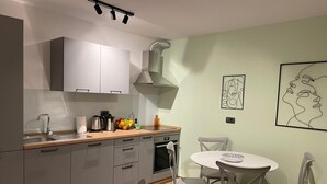 A compact kitchen with a sink, stove, and cabinets, a dining area with a table and chairs, and artwork on the walls. - Apartment Niccolo - Duplex Apartment with Sea View (Fazana)