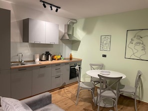 A compact kitchen with a sink, stove, and cabinets, a dining area with a table and chairs, and artwork on the walls. - Apartment Niccolo - Duplex Apartment with Sea View (Fazana)