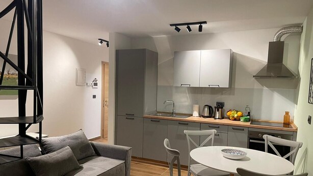 A modern kitchen with grey cabinets, a white countertop, and a dining area with a round table and chairs. - Apartment Niccolo - Duplex Apartment with Sea View (Fazana)