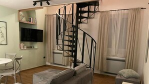 A living room with a grey sofa, a white table, a black spiral staircase, and a TV mounted on the wall. - Apartment Niccolo - Duplex Apartment with Sea View (Fazana)