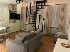 A living room with a grey sofa, a white table, a black spiral staircase, and a TV mounted on the wall. - Apartment Niccolo - Duplex Apartment with Sea View (Fazana)
