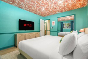 Una stanza con pareti color verde acqua, un letto con lenzuola bianche, una TV a parete e una porta che dà su un'altra stanza.
