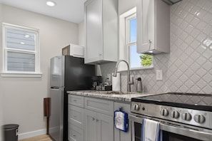 A kitchen with white cabinets, a stainless steel stove, a coffee maker, and a window with blinds. - Casita w/ Outdoor Shower, Near Main + Wineries! (Fredericksburg)