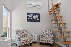 A room with patterned chairs, a world map artwork, a white air conditioner, and a wooden spiral staircase. - Casita w/ Outdoor Shower, Near Main + Wineries! (Fredericksburg)