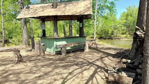 A rustic wooden structure with a green bench, surrounded by trees and a body of water. - 2-bedroom waterfront camper in welcoming Decaturville with AC for relaxing stays (Decaturville)