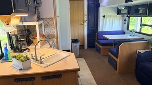 A compact RV interior with a kitchenette, a sink, a coffee maker, a trash can, and a seating area with a table and cushions. - 2-bedroom waterfront camper in welcoming Decaturville with AC for relaxing stays (Decaturville)