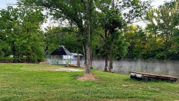 A grassy area with a small building, a tree, and a body of water. - 2-bedroom waterfront camper in welcoming Decaturville with AC for relaxing stays (Decaturville)