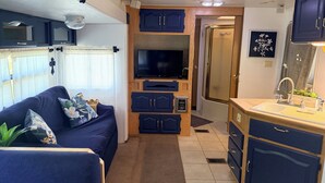 A compact RV interior with a sofa, TV, cabinets, and a sink. - 2-bedroom waterfront camper in welcoming Decaturville with AC for relaxing stays (Decaturville)