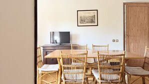 Ein Essbereich mit Holztisch und Korbstühlen, einem Fernseher auf einem Holzschrank und einem gerahmten Bild an der Wand.