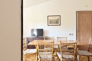 Ein Essbereich mit Holztisch und Korbstühlen, einem Fernseher auf einem Holzschrank und einem gerahmten Bild an der Wand.