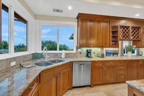 A kitchen with wooden cabinets, a stainless steel dishwasher, granite countertops, and a view through large windows. - Walk to the Shore from This Point Richmond Escape (Richmond)