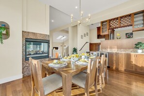 A dining area with a wooden table set for six, a fireplace, and a kitchen with wooden cabinets and a marble countertop. - Walk to the Shore from This Point Richmond Escape (Richmond)