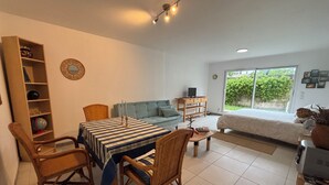 Uma sala de estar moderna com uma mesa de jantar, cadeiras, um sofá, um rack de TV e uma grande janela com vista para o verde.