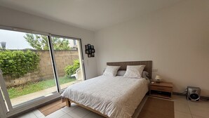 Quarto com cama, mesa de cabeceira, alto-falante e porta de vidro deslizante para uma varanda.