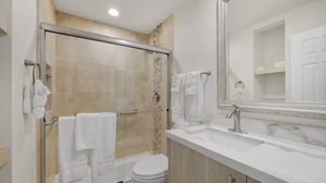 A modern bathroom with a glass shower enclosure, a white toilet, and a large mirror above a sink. - Indian Palms Intervals for May (Indio)