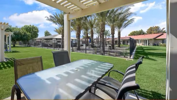 An outdoor patio with a table and chairs, surrounded by a fence and palm trees. - Indian Palms Intervals for May (Indio)