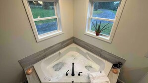 A corner bathroom with a bathtub, two windows, a potted plant, and a towel.