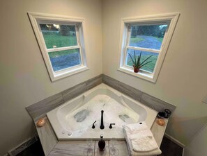 Une petite salle de bain avec une baignoire, deux fenêtres, une plante en pot et une serviette.