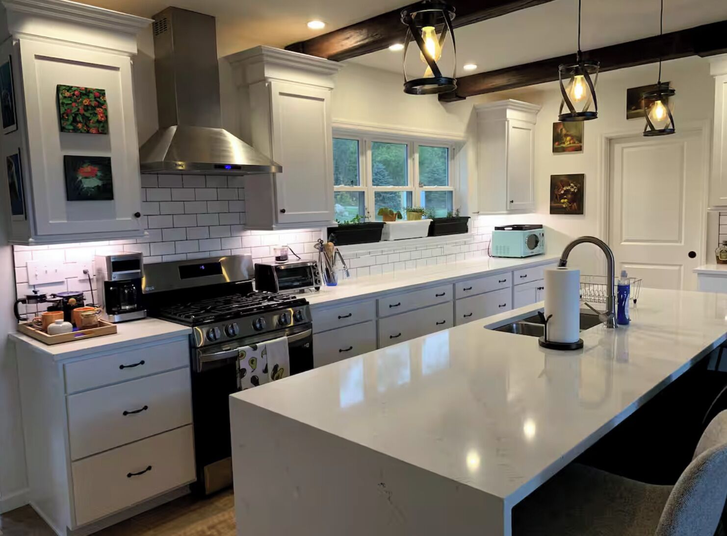 A modern kitchen with white cabinetry, a large island, a stove, and a coffee maker.