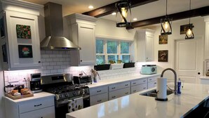 A modern kitchen with white cabinetry, a large island, a stove, and a coffee maker.