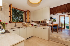 Eine Küche mit großem Fenster, Holzschränken, einer Spüle und einem Essbereich mit Stühlen.