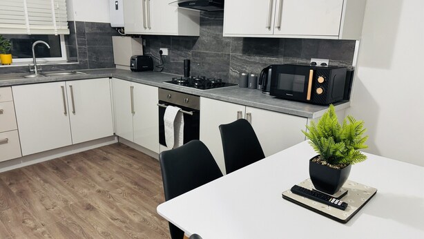Eine moderne Küche mit weißen Schränken, einer schwarzen Arbeitsplatte, einer Mikrowelle und einem kleinen Blumentopf auf dem Tisch.